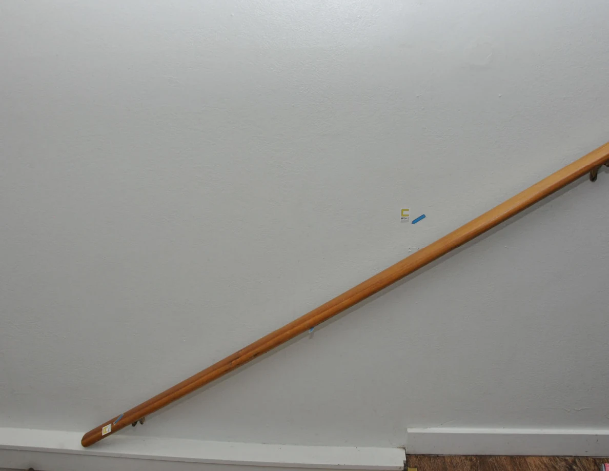 Wider view of wooden handrail, pale wall and label C with blue arrow.