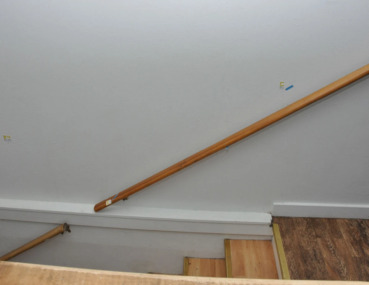 Wooden handrail and pale stairwell wall with small labels and blue arrows.