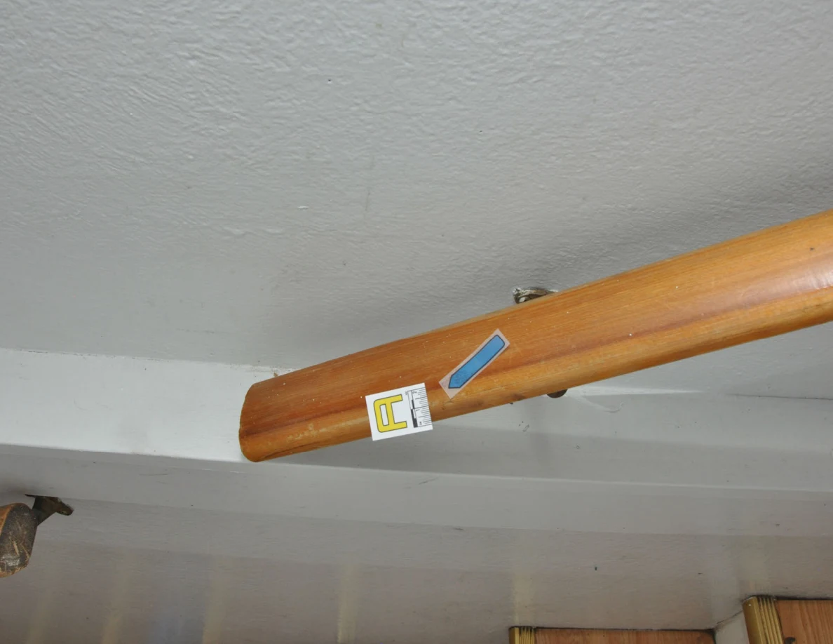 Closer view of a wooden handrail end with a letter label and blue arrow.