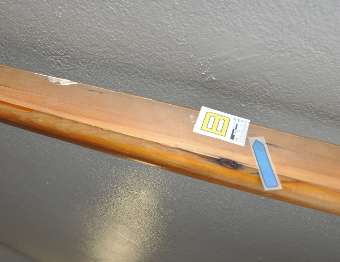 Letter label B and blue arrow on a wooden handrail beside scuffed wall paint.