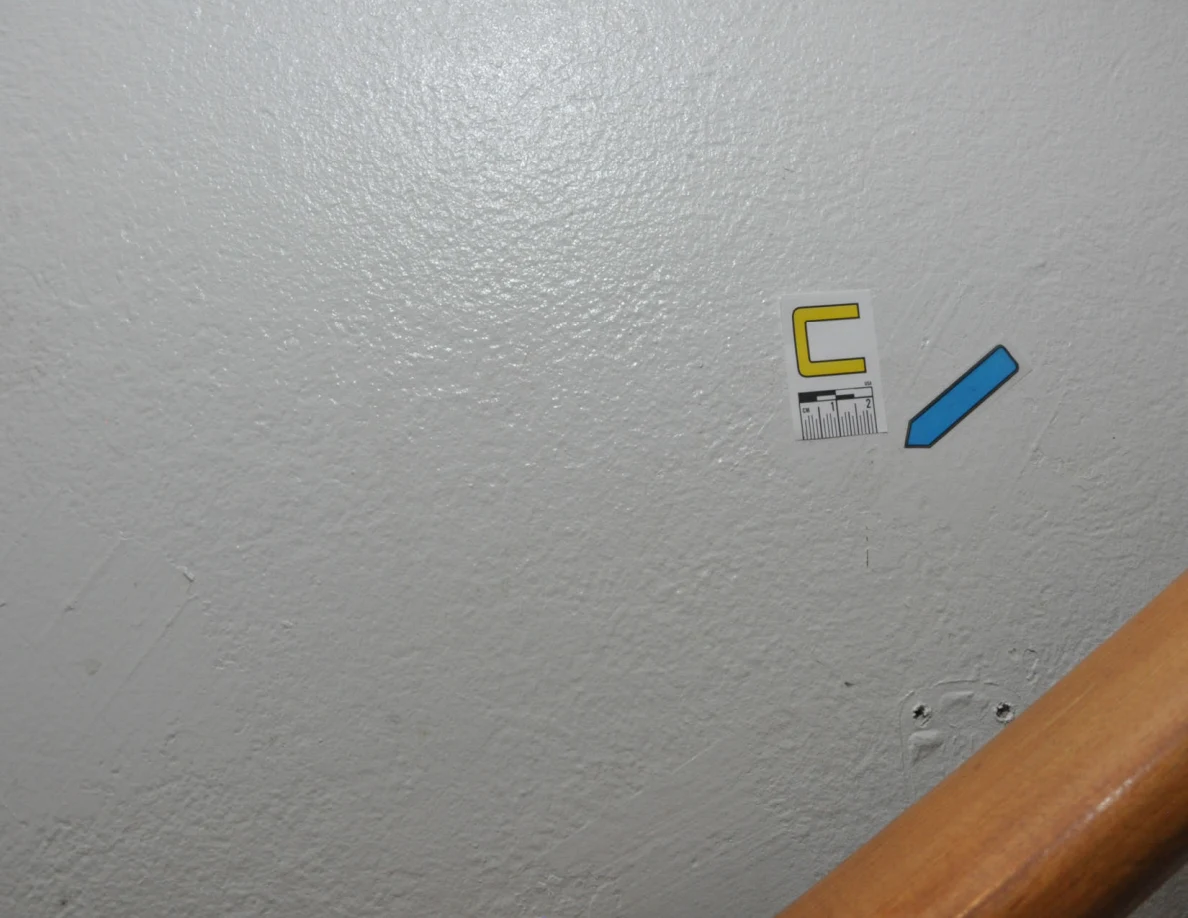 Letter label C and blue arrow on a textured wall above a wooden handrail.