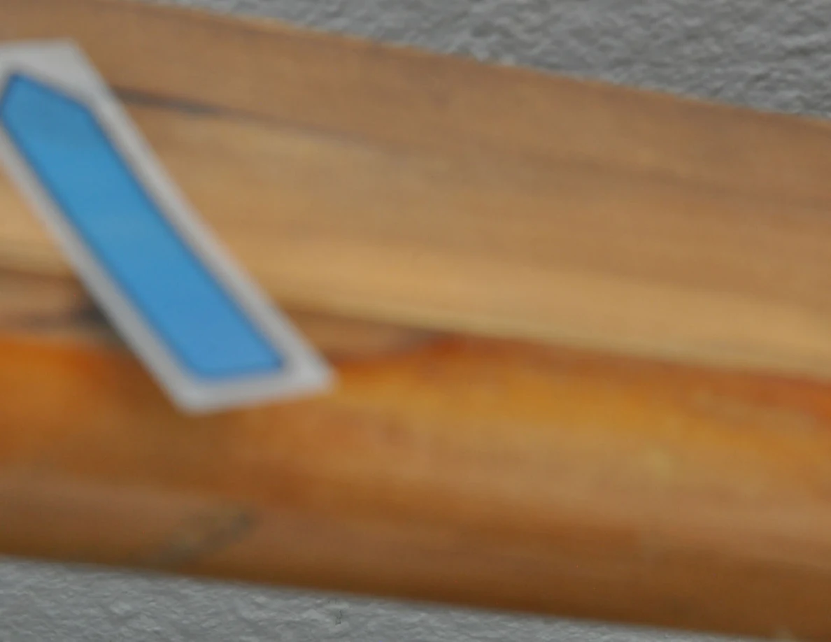 Blurred close view of a wooden handrail and blue arrow beside a reddish wood mark.