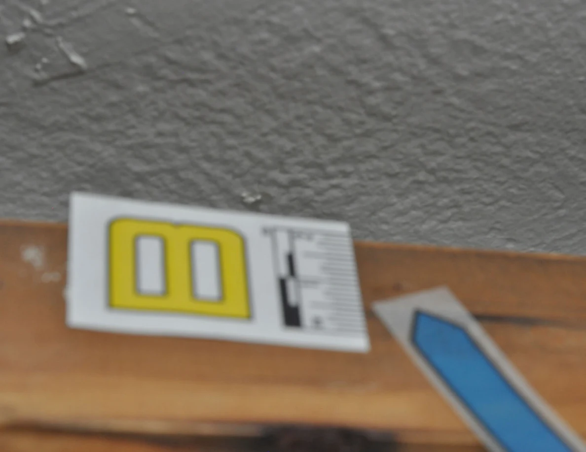 Soft-focus view of label B and blue arrow on a wooden handrail.