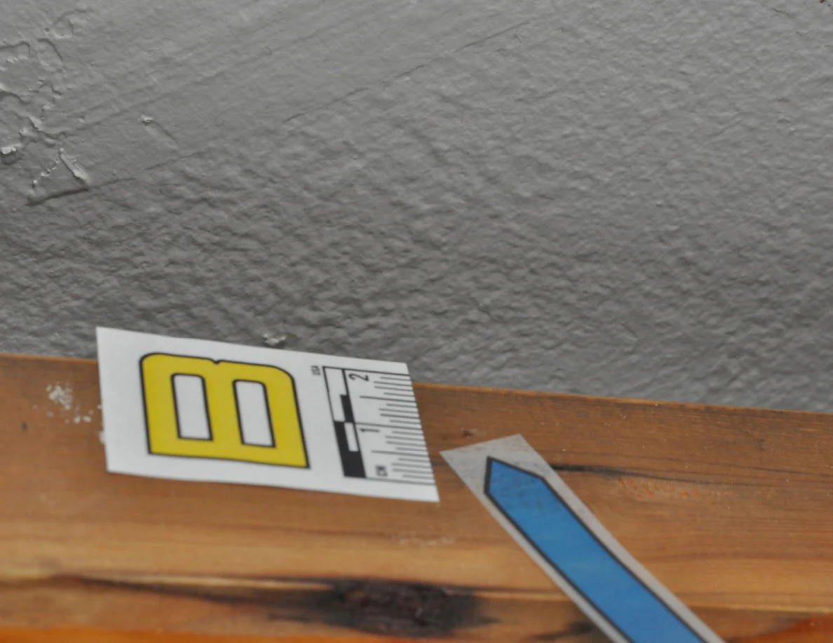 Wider close view of label B, blue arrow and dark discoloration along a wooden handrail.