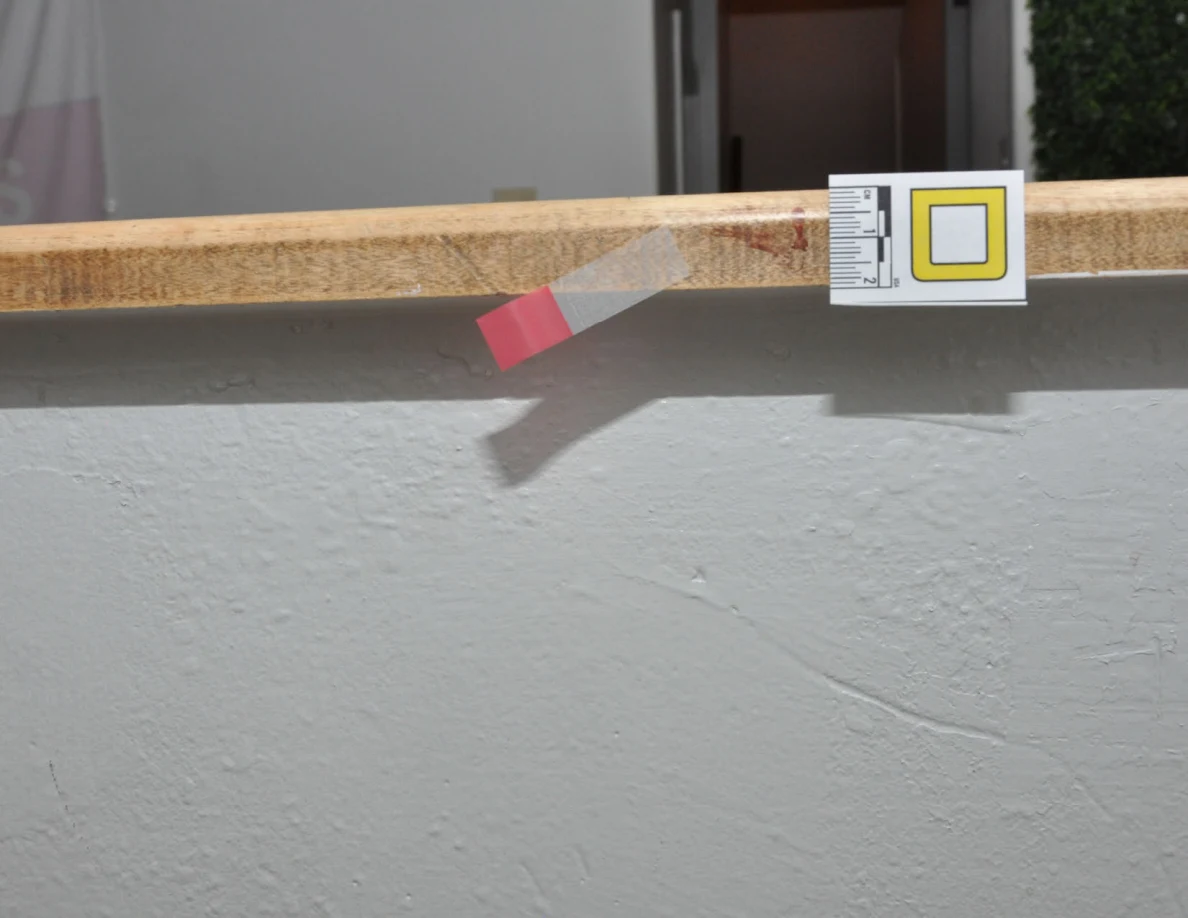 Letter label and pink tape beside a reddish mark along a wooden half-wall cap.
