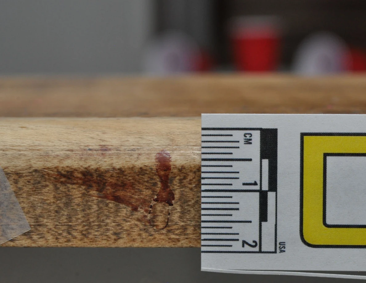 Close view of a reddish mark on the edge of a wooden cap beside a measurement label.