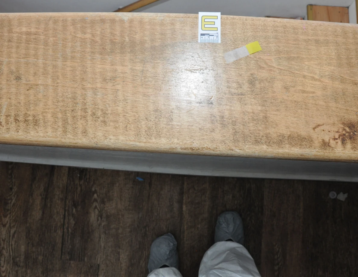 Letter label E and yellow tape on a worn wooden half-wall cap.