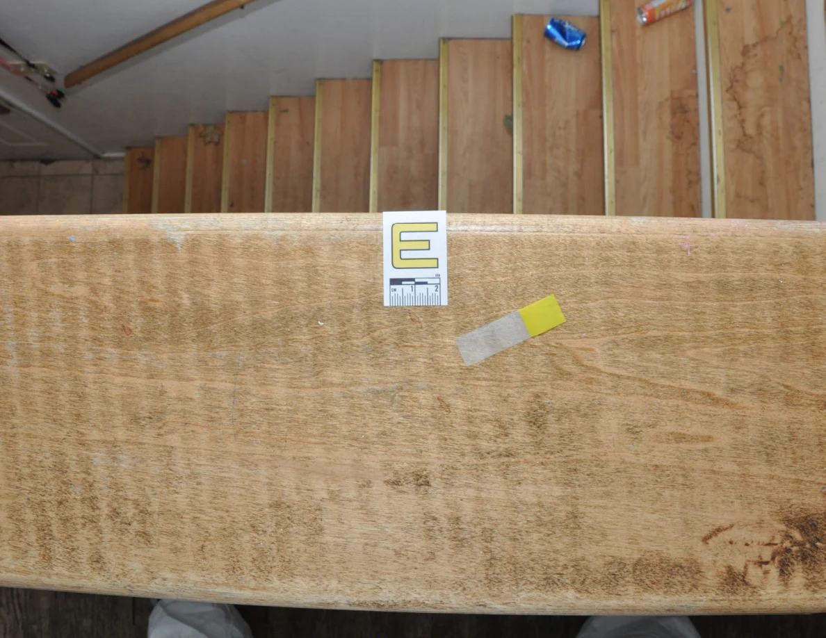 Overhead view of label E and yellow tape on a wooden cap above stairs with drink cans.
