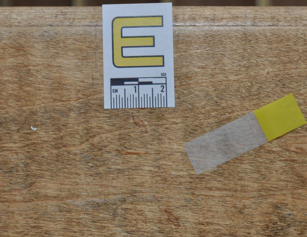 Close view of label E, yellow tape and faint reddish marks on wood grain.