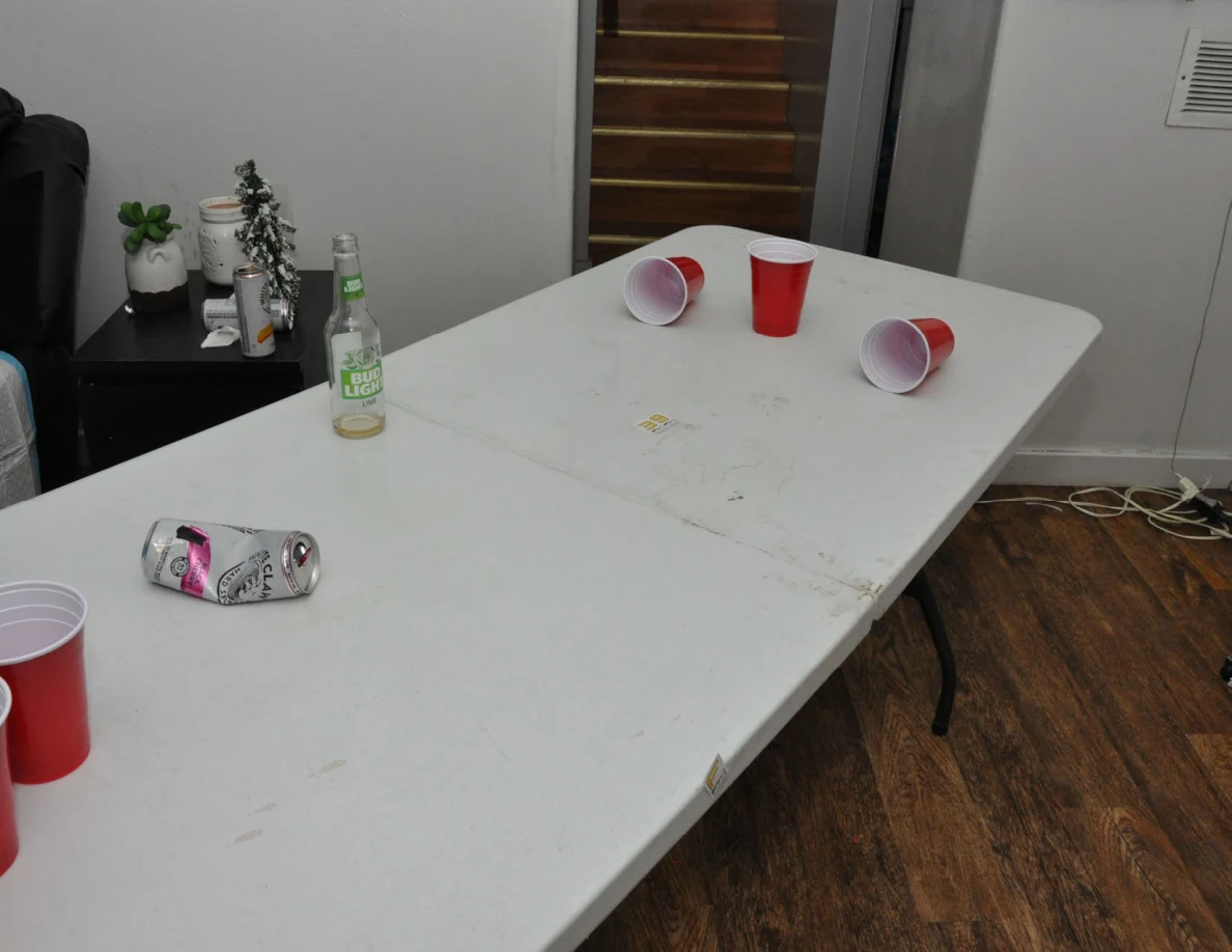 White folding table with scattered red plastic cups, a drink can and a clear bottle.
