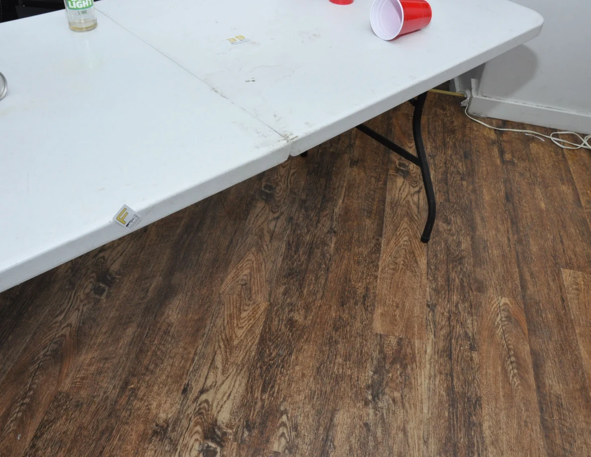 White folding table edge and legs over wood-look flooring, with a letter label on the edge.