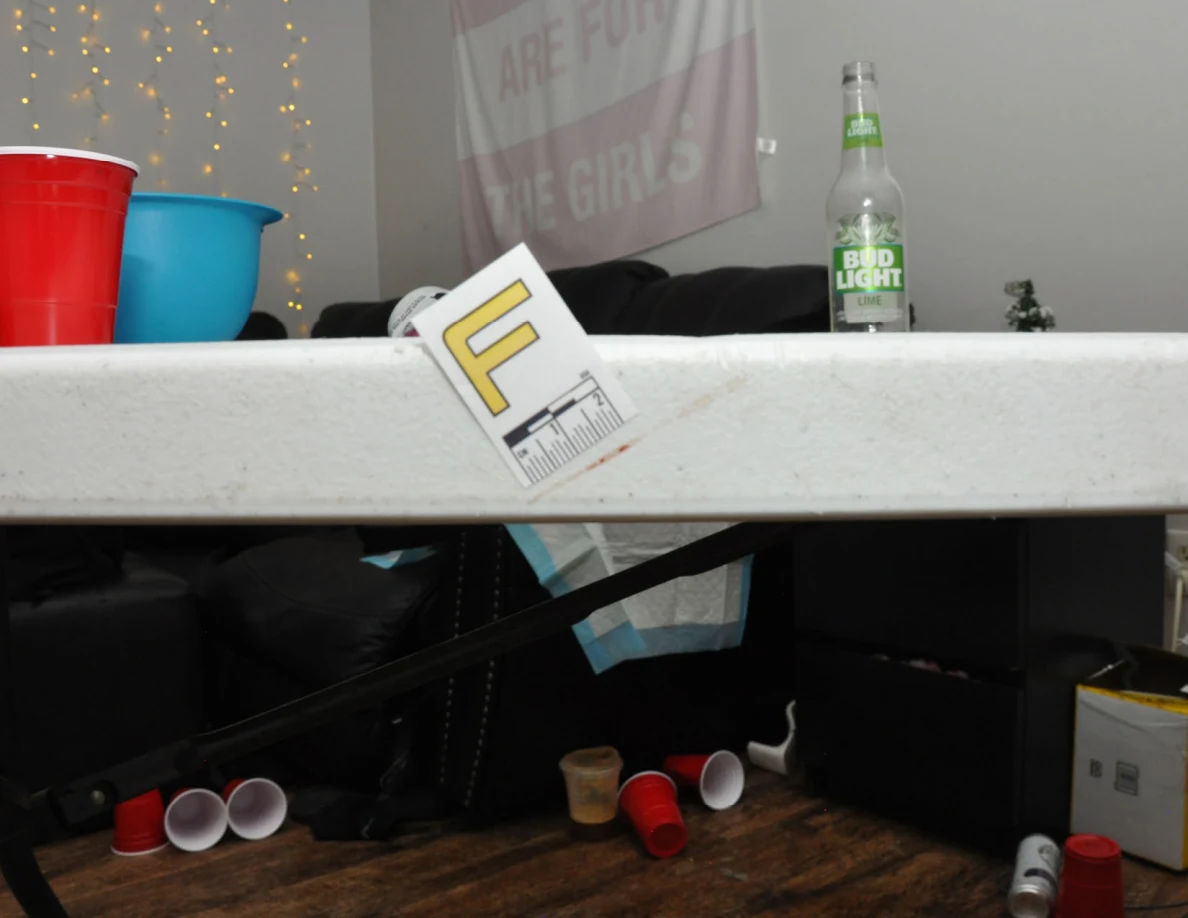 Letter label F on a white table edge, with red cup, blue bowl and clear bottle above.