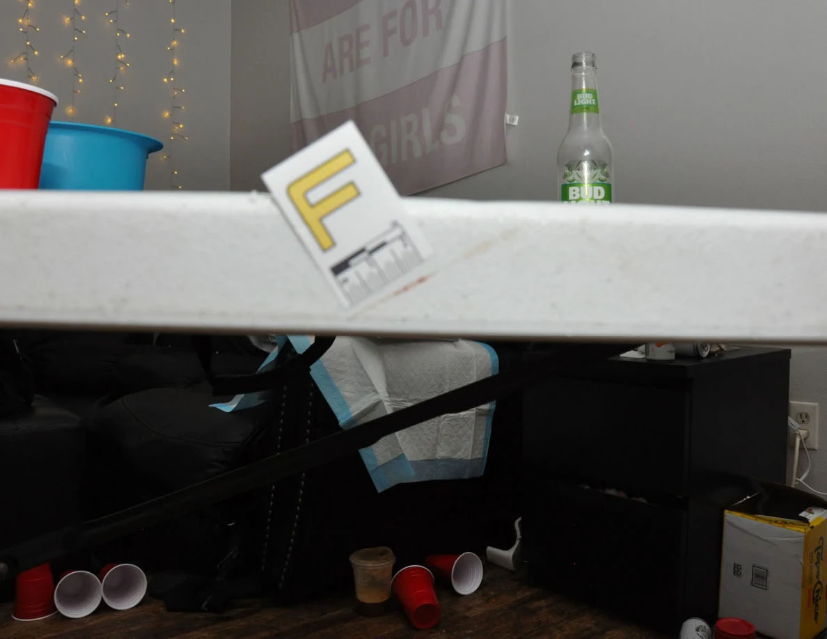 Side view of label F on a white table edge, with sofa and scattered cups behind.
