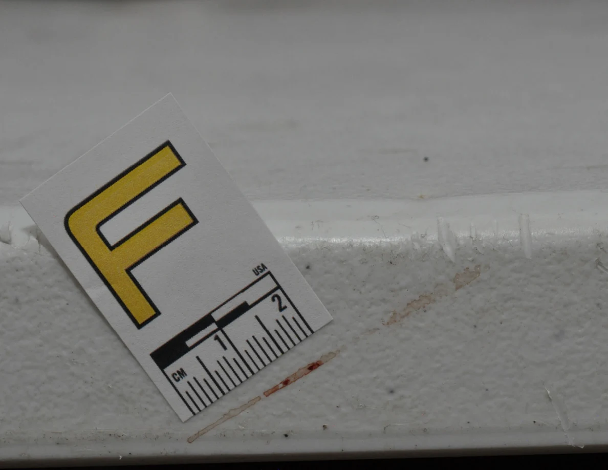 Close view of label F beside a reddish streak along the edge of a white table.