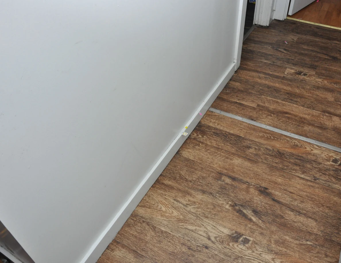 Angled view of hallway wall, baseboard markers and a metal floor threshold.