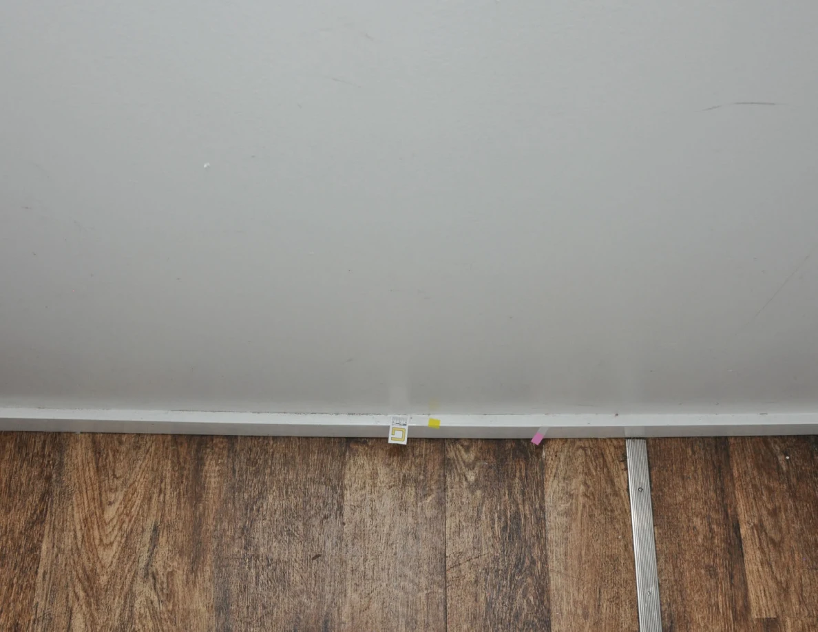 Pale lower wall with small labels and yellow and pink tape along the baseboard.