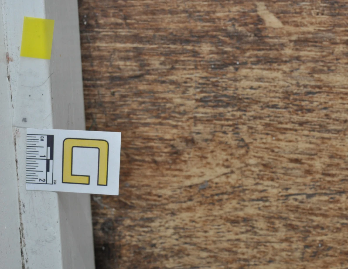 Rotated close view of a baseboard measurement label and yellow tape beside wood-look floor.