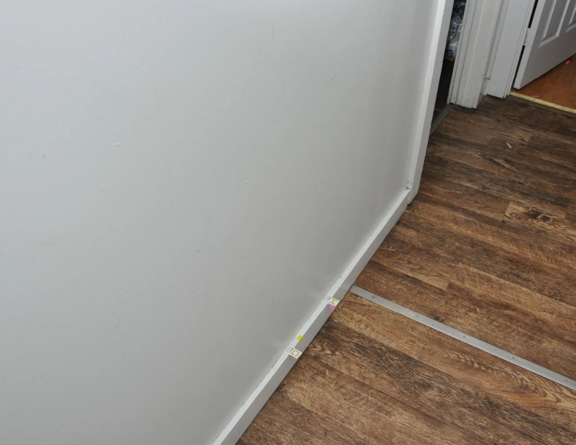Hallway wall and baseboard with small labels near a doorway.