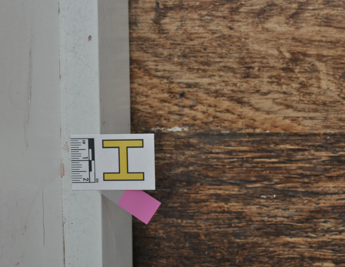 Close view of baseboard label and pink tape beside faint reddish marks.