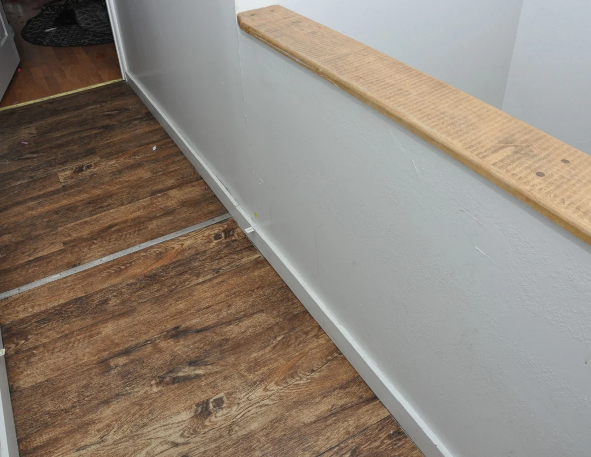 Wood-capped half-wall beside wood-look hallway floor and doorway.