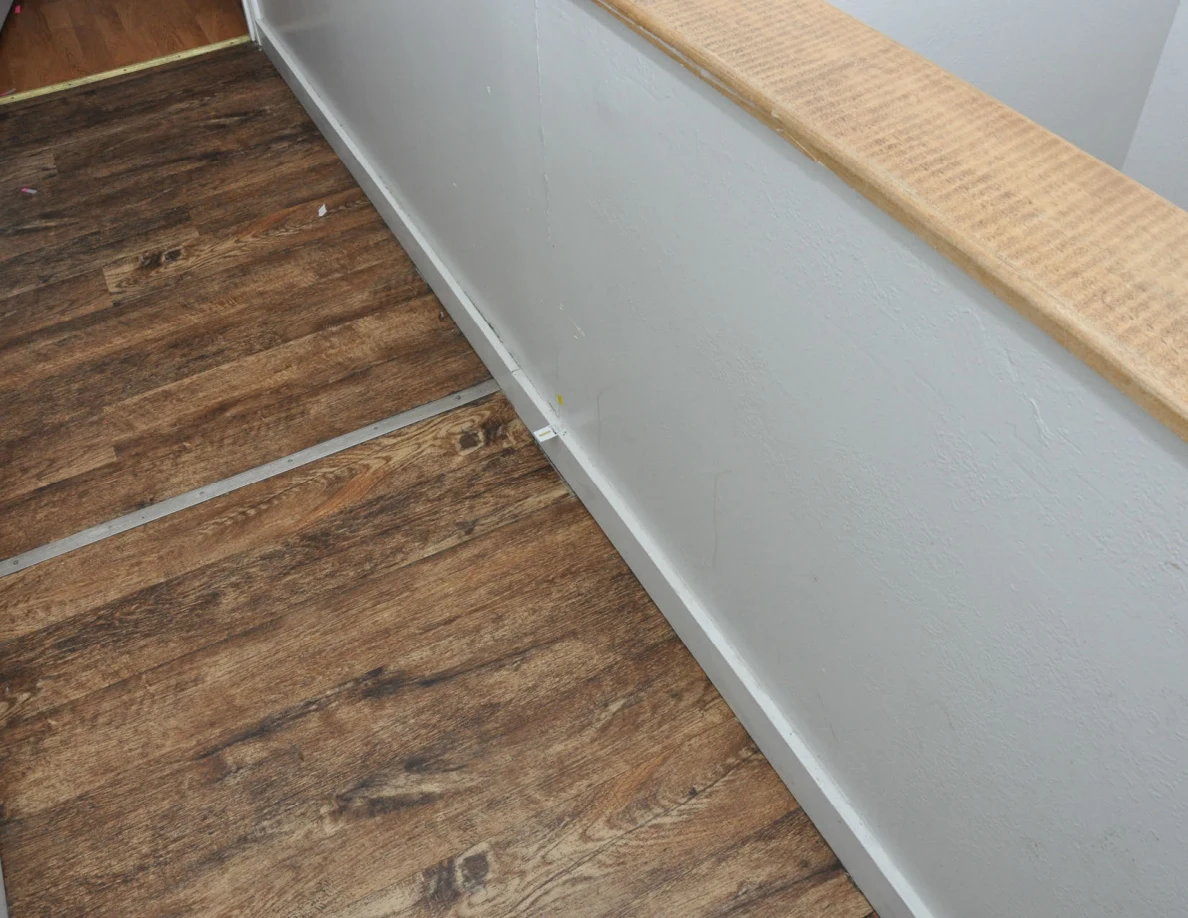 Angled view along a pale half-wall with wooden cap and white baseboard.