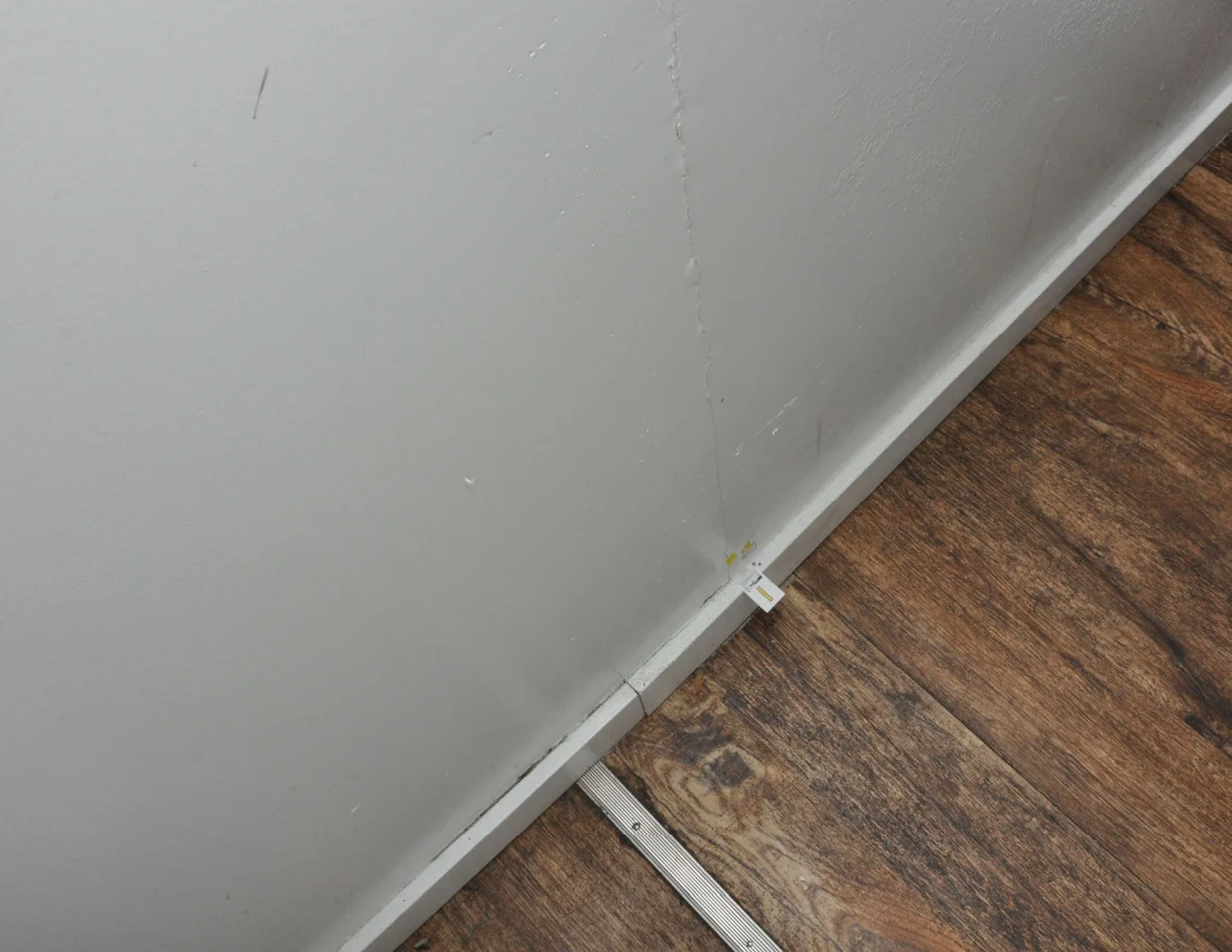 Angled view of a wall crack and scuffs above a white baseboard.