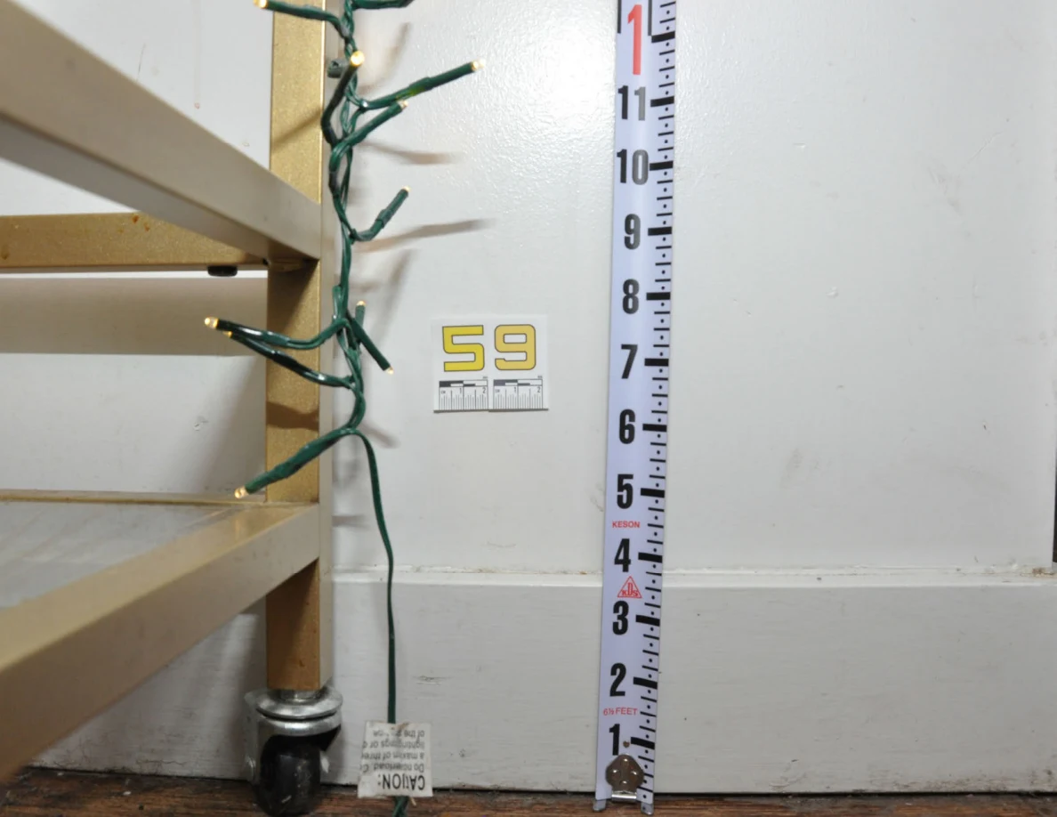 Wider view of label 59, measuring tape and gold cart frame beside baseboard.