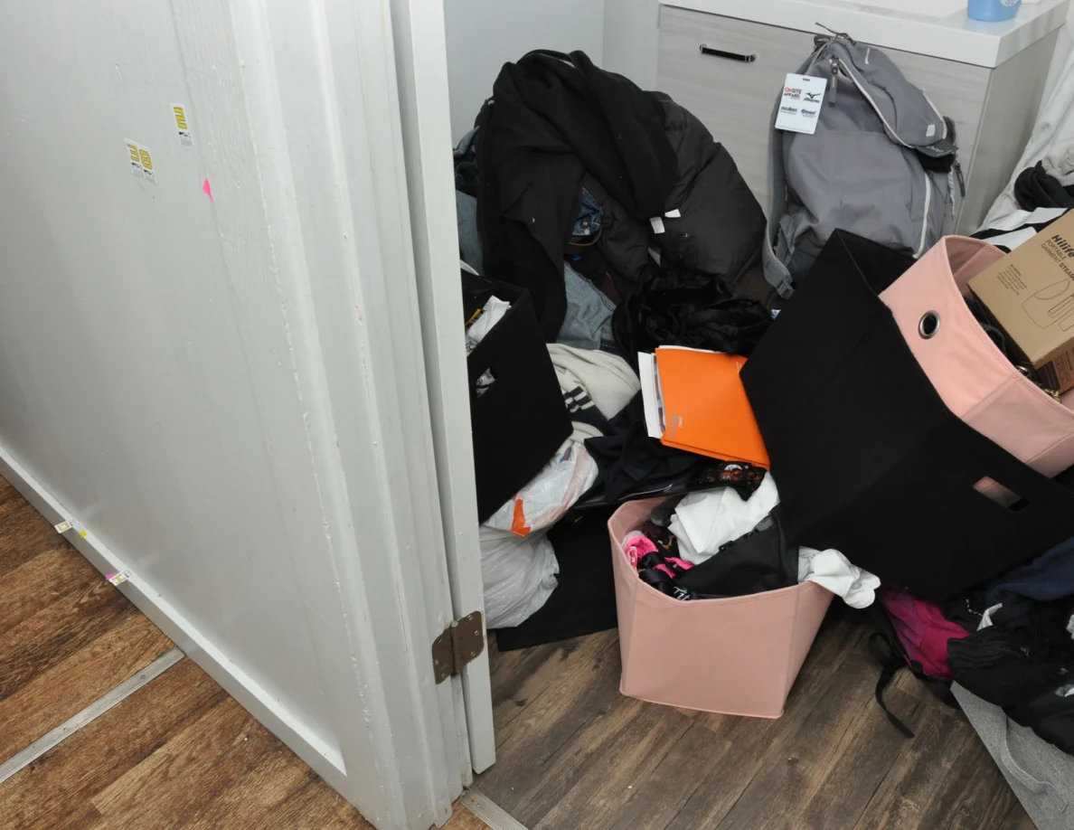 Doorway wall with small labels and pink tape beside clothing-filled bins and backpack.