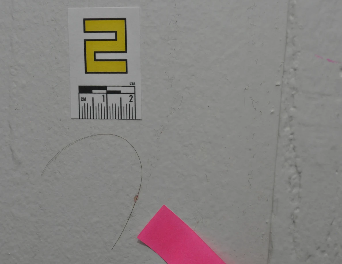 Close view of label 2, a curved strand and pink tape on a textured wall.