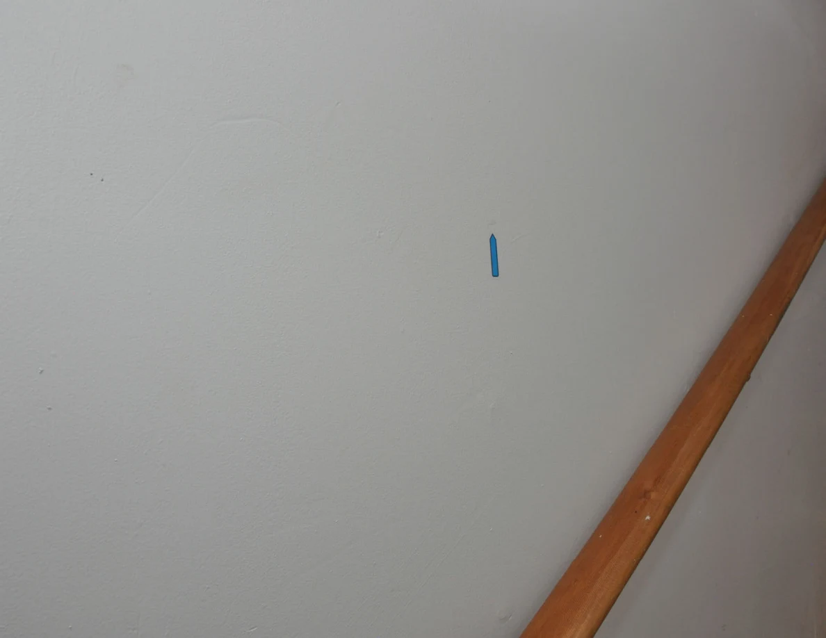 Blue arrow sticker on pale stairwell wall above a wooden handrail.