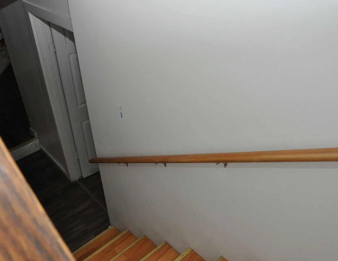 Angled view down a stairwell with wooden handrail and small blue wall marker.