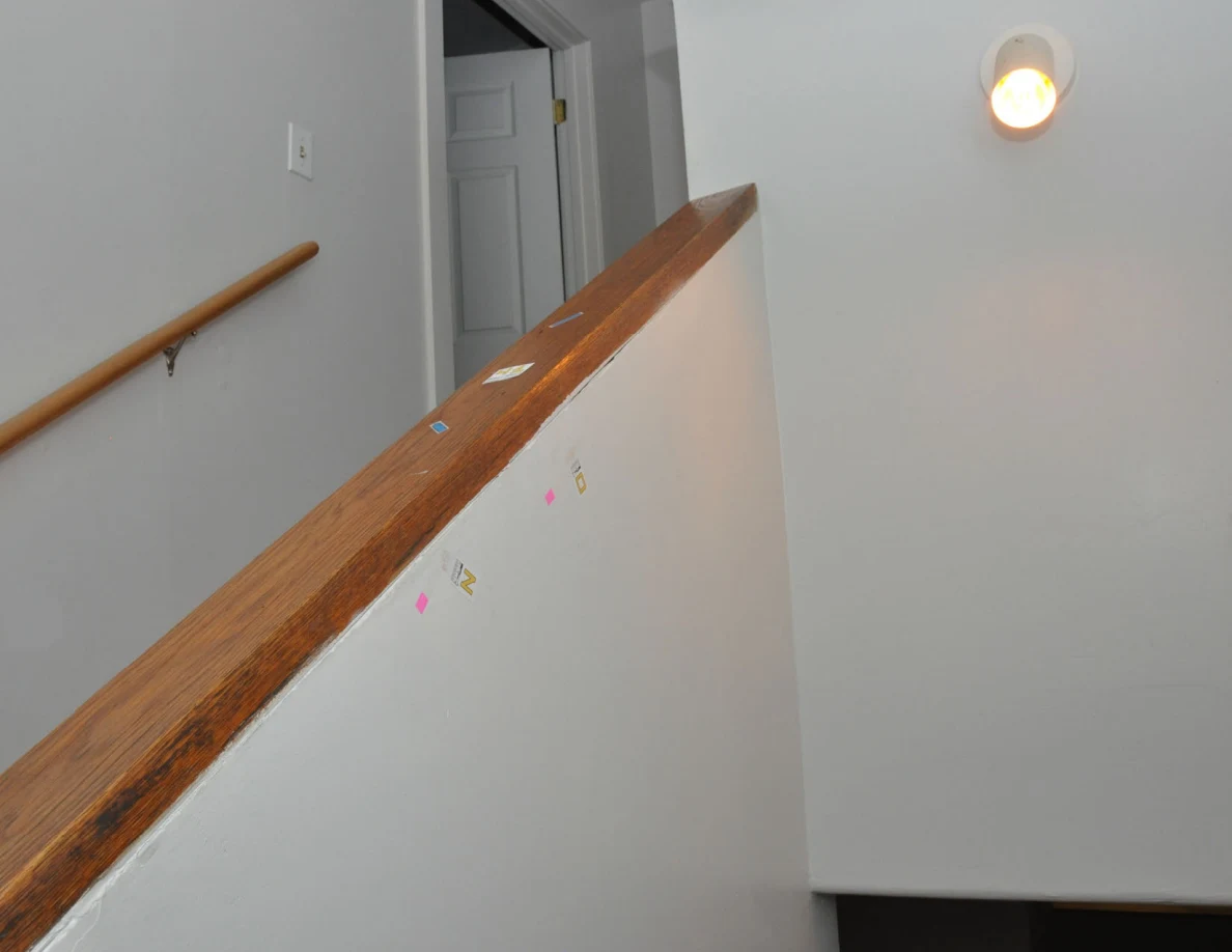 Wood-capped half-wall with letter labels and pink tape beside a wall light.