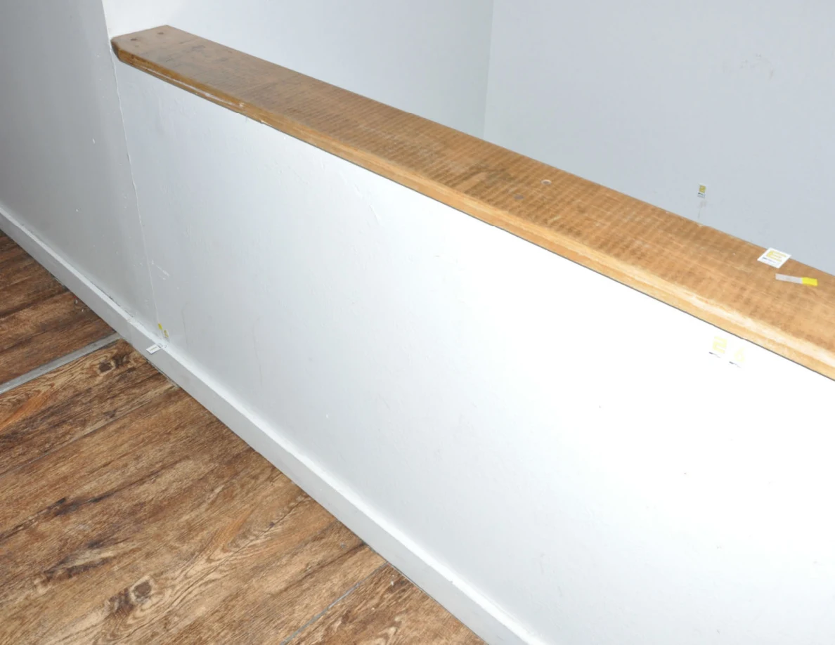 Wide view of a wood-capped half-wall beside wood-look flooring with small evidence labels.