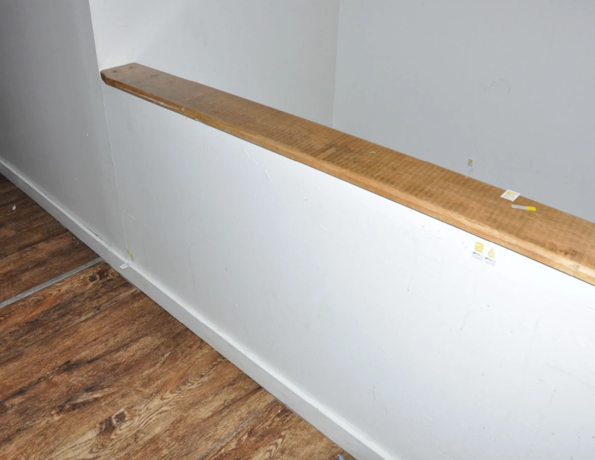 Wood-capped half-wall with small labels and faint marks above wood-look flooring.