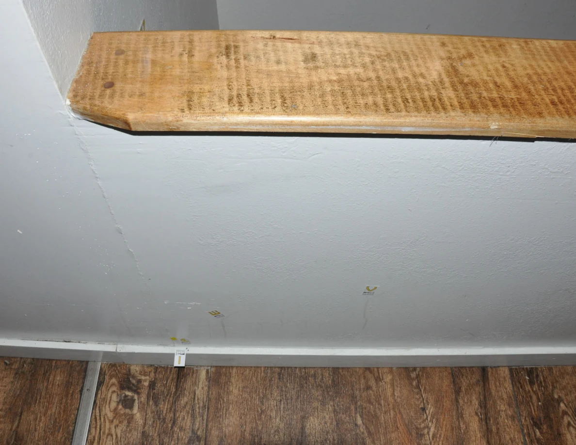 Wood-capped half-wall with labels near two faint streaks and a wall crack.