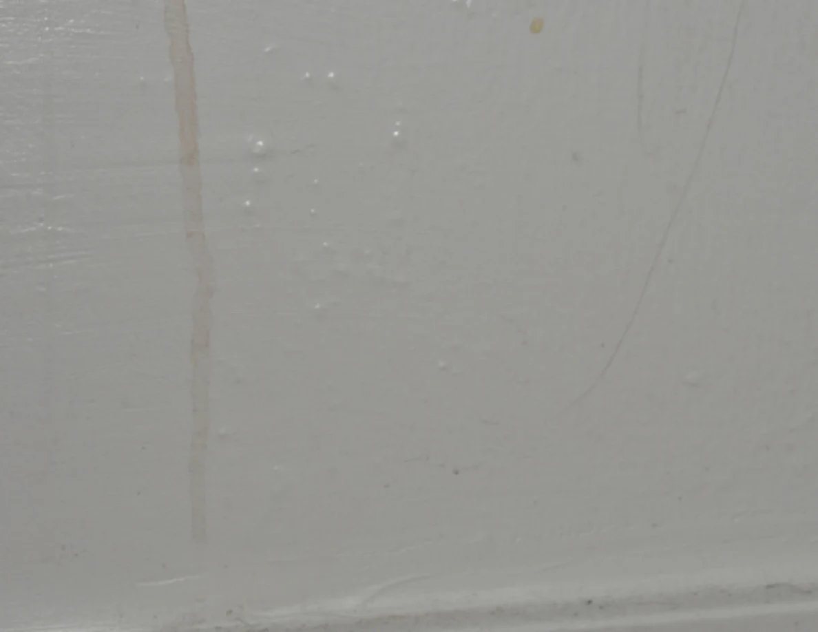 Lower end of a faint tan streak near a white baseboard.