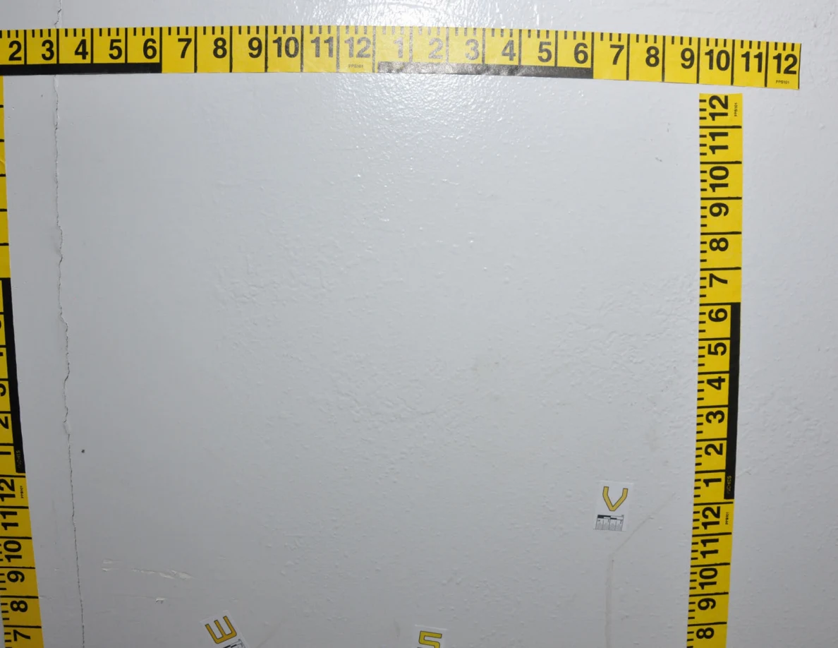 Closer view of a wall area bordered by yellow measurement tape with labels near faint marks.