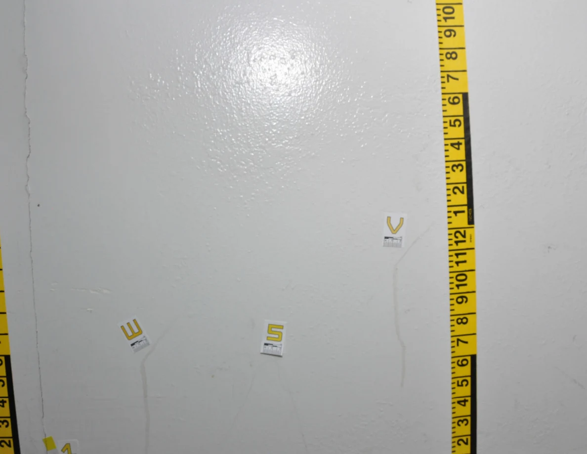 Pale wall framed by yellow measurement tape with labels W, S and V near faint vertical streaks.