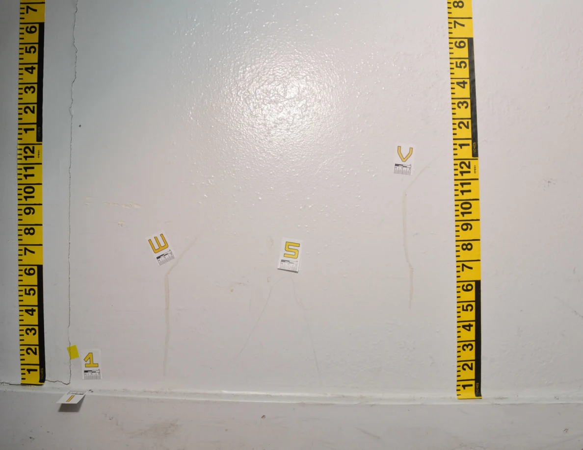 Wider view of a wall rectangle outlined in yellow measurement tape, with small labels beside marks and a crack.