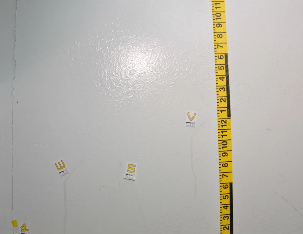 Closer view of labels W, S and V near a wall crack and yellow measurement tape.