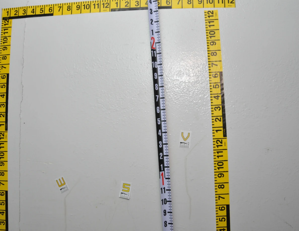 Wall area bordered with yellow measurement tape, a black-and-white measuring rod and labels W, S and V.