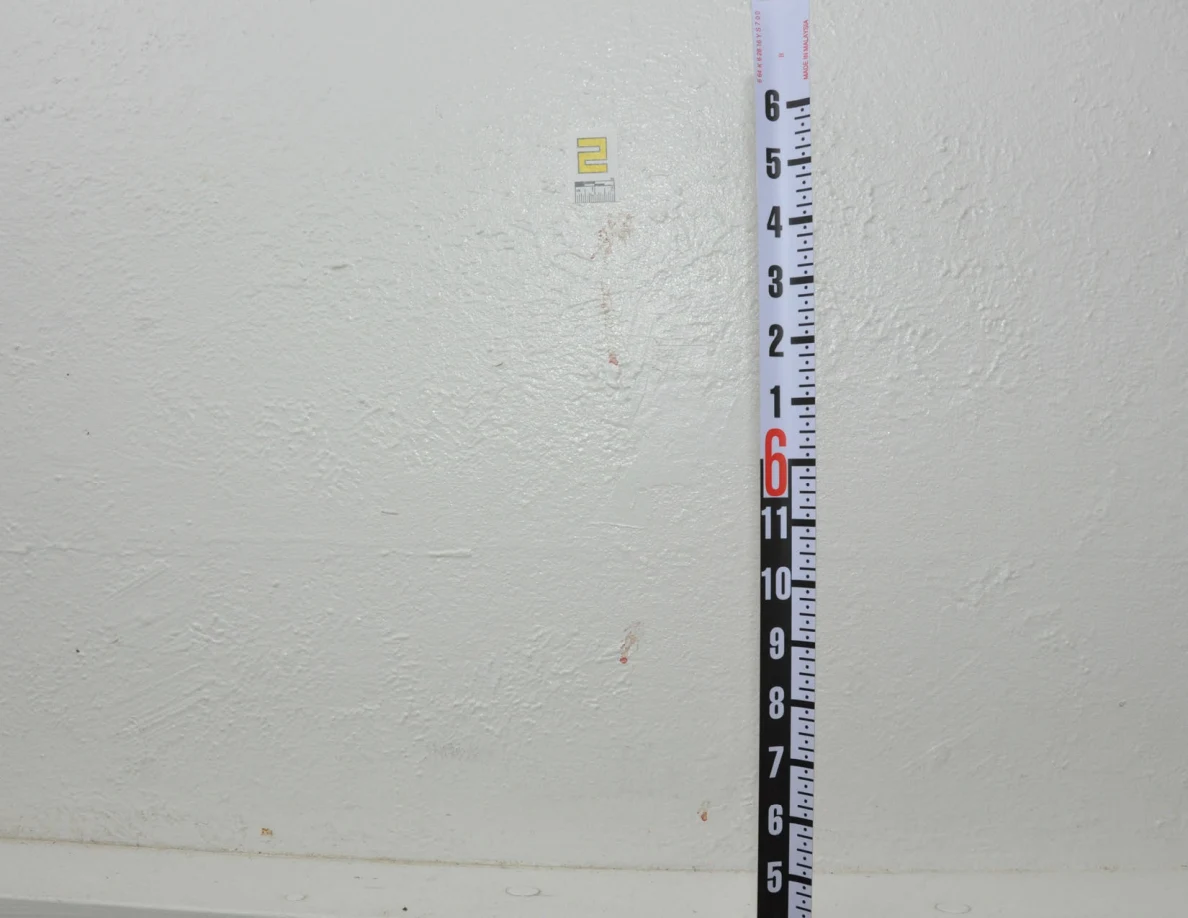 Small yellow label and reddish wall streaks beside a vertical black-and-white measuring rod.