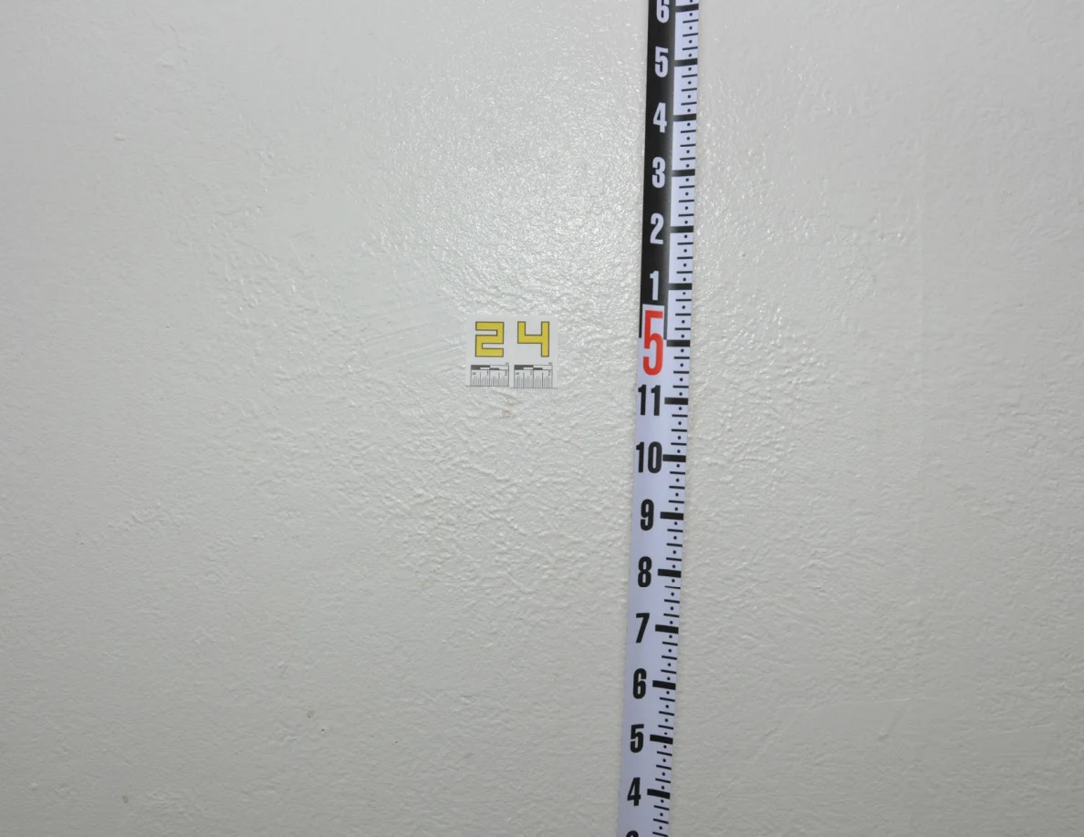 Label 24 beside a vertical black-and-white measuring rod on a pale wall.