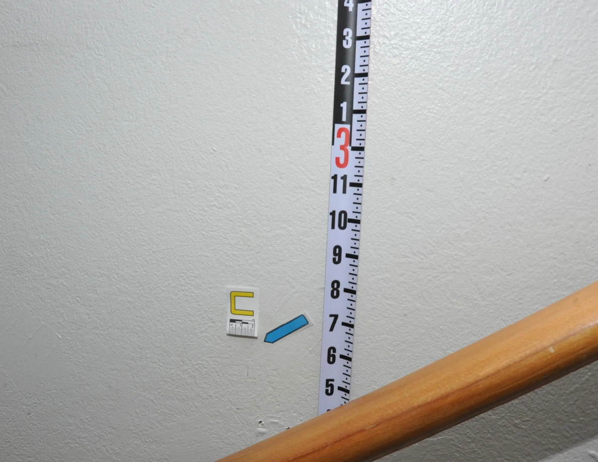Letter C and a blue arrow beside a vertical measuring rod above a wooden handrail.