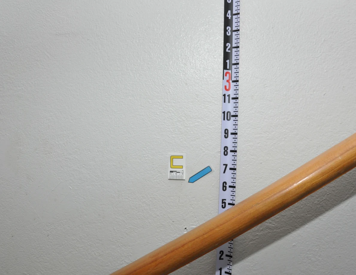 Angled view of letter C and a blue arrow beside a measuring rod and wooden handrail.