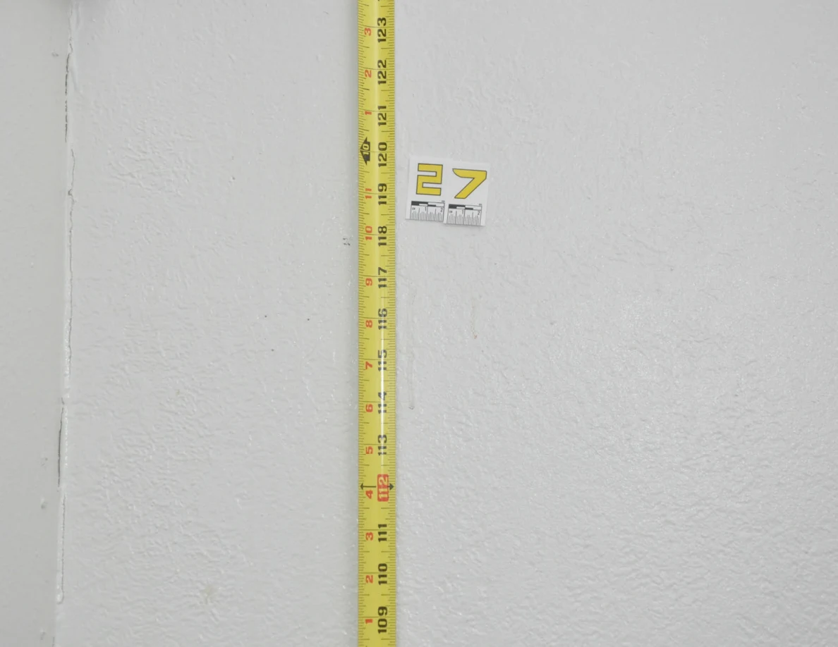 Label 27 beside a vertical yellow tape measure near a wall corner.