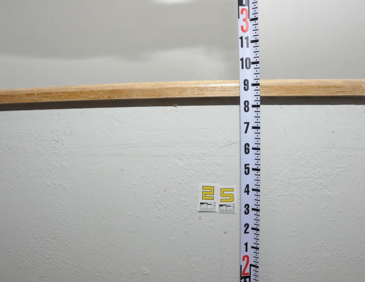 Label 25 beneath a wooden cap beside a vertical black-and-white measuring rod.