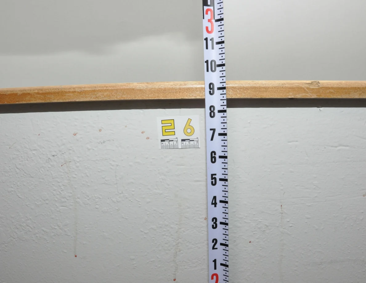 Reddish streaks and label 26 beneath a wooden cap beside a vertical measuring rod.