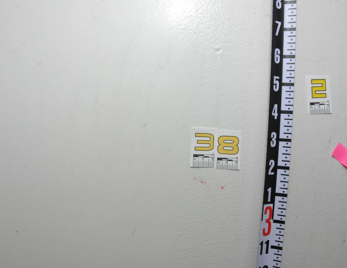 Labels 38 and 2 beside a vertical measuring rod and small pieces of pink tape on a wall.