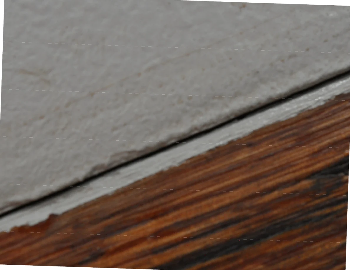 Close view of a wooden cap meeting a white wall, with a tan mark on the paint and a dark seam.